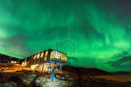 Schöne Aussicht auf Aurora borealis, Nordlichter, die über Luxushotels glühen und männliche Touristen, die im Winter auf dem Berg Hengill in Nesjavellir, Island, genießen