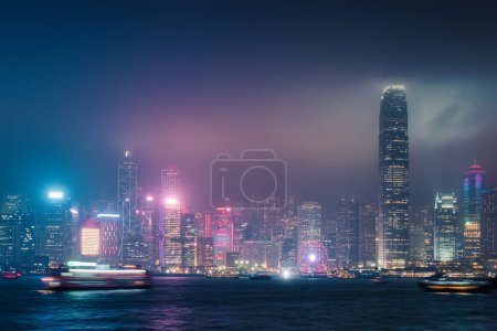 Beautiful night scene cityscape of colorful illuminated business skyscraper building with laser lighting show on Victoria Harbour in foggy day at Hong Kong island 