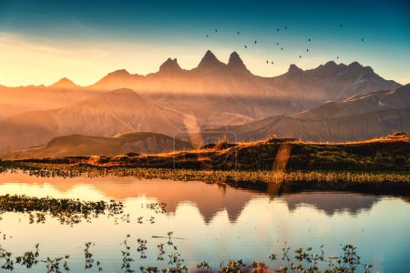 Picturesque landscape of sunrise shines over Lac Guichard with bird flying on Arves massif and lake reflection in autumn at Aiguilles d Arves, French Alps, Savoie, France