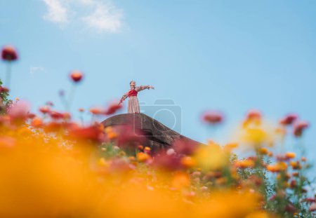 Cheerful beautiful asian woman standing on the rock among the Straw flower or Everlasting flower blooming in the field at Phu Hin Rong Kla national park, Thailand