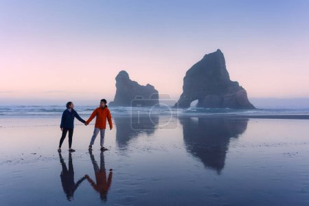Asian couple enjoying on Wharariki beach with iconic archway island at Cape Farewell, New Zealand