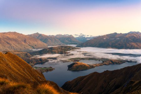 Téléchargez les photos : Breathtaking landscape of sunrise shining over summit of Roys Peak and foggy mountain over Lake Wanaka in autumn at New Zealand - en image libre de droit