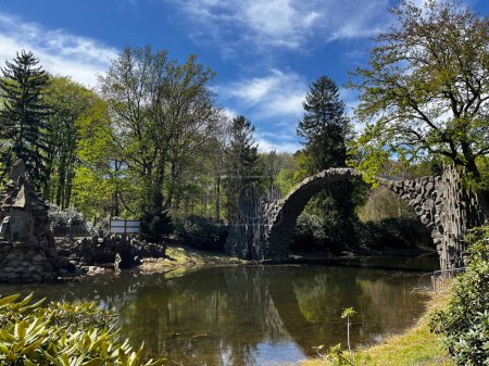 Schöner See mit einer steinernen halbkreisförmigen Brücke, klares sauberes Wasser im See, grüne Bäume ringsum, Natur, Landschaft