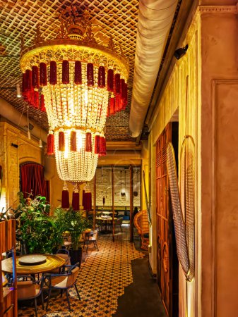 Dieses luxuriöse Interieur verfügt über einen großen Kronleuchter mit roten und klaren Kristallen, der einen opulenten Raum erhellt. Elegante Möbel, aufwändige Wandgestaltung und Zimmerpflanzen schaffen ein Ambiente 