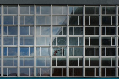 Ein minimalistisches modernes Gebäude mit einem symmetrischen Raster quadratischer Fenster, das den blauen Himmel und die städtische Umgebung reflektiert.