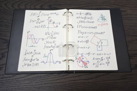 Das Bild zeigt ein Notizbuch voller komplexer mathematischer Gleichungen und farbenfroher Graphen, die auf fortgeschrittene mathematische Studien hindeuten und auf einer dunklen Holzoberfläche platziert sind..