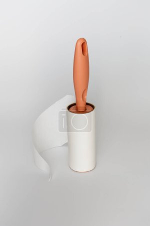 A lint roller with a peach handle is captured mid-use, with a sheet partially peeled off, against a white background. The image highlights the simplicity and functionality of the everyday cleaning too