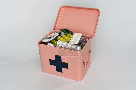  Ein rosafarbener Erste-Hilfe-Kasten mit einem schwarzen Kreuz ist geöffnet und zeigt verschiedene Medikamente und Nahrungsergänzungsmittel. Gut bestückt mit Blisterverpackungen mit Pillen, Kapseln und Tabletten für den medizinischen Notfall.