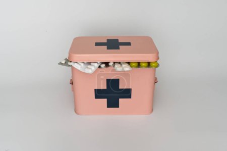 Ein rosafarbener Erste-Hilfe-Kasten mit schwarzem Kreuz zeigt verschiedene Medikamente und Nahrungsergänzungsmittel.