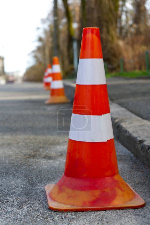 Téléchargez les photos : Une ligne de cônes orange vif se dresse sentinelle sur une rue asphaltée, marquant une frontière ou une zone réglementée. Leur couleur vive assure la visibilité, avertissant les passants. - en image libre de droit
