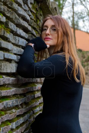 Téléchargez les photos : Une personne se penche contre un mur de pierre recouvert de mousse, créant un sentiment de mystère et d'anonymat. La scène est à l'extérieur, entourée de verdure, et évoque un sentiment de solitude et d'introspection. - en image libre de droit