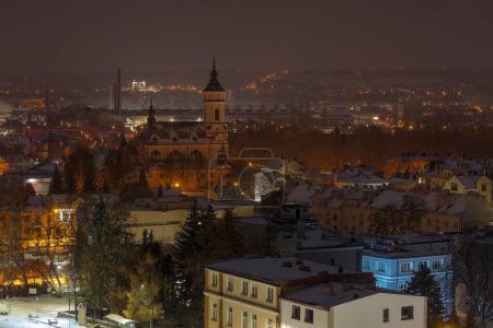  Ostrowiec Swietokrzyski bei Nacht unter dem Schnee. Stiftskirche des Erzengels Michael. Die nächtlichen Lichter der Stadt leuchten schön auf dem verschneiten Hintergrund. Auf dem Hügel kann man die beleuchtete Kirche in der benachbarten Stadt (Szewna) sehen.).  