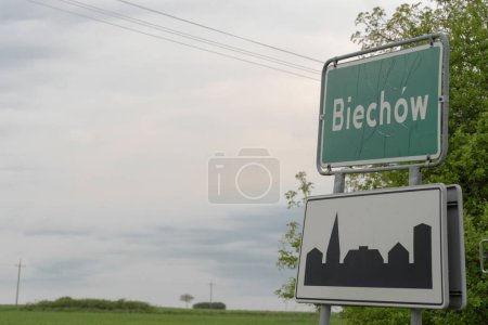 .Una junta - área construida - y otra con el nombre de la ciudad (Biechow). Un cielo gris nublado en el fondo. Una placa frente a la entrada del pueblo con hojas frescas de primavera y un cielo nublado en una tarde de mayo. 