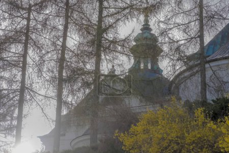 Die Kirche St. Michael auf dem Hügel im zeitigen Frühling. Eine historische Kirche mit einem Turm mit einem Dach aus Kupferblech zwischen Bäumen und blühenden Büschen im Frühling an einem nebligen Tag unter grauem Himmel. Tempel