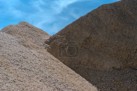 Heap of dry brown gravel in gravel pile on a white background, close - up.A large pile of gravel on a construction site under a blue sky. Road construction site. A large supply of building materials - gravel in large quantities .  