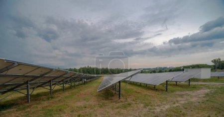  .Cloudy sky above a photovoltaic panel farm. A whole battery of solar panels generating electricity over a large area under a dramatically and picturesque cloudy sky. Solar power plant near the city in the background with skyscrapers down town .  