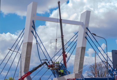 Foto de Polonia Ostrowiec Swietokrzyski 18 de abril, 11: 55. Grúa Magni en el sitio de construcción del puente. Construcción de un puente colgante sobre el río Kamienna. Tornillo y tensado de las cuerdas de soporte. - Imagen libre de derechos
