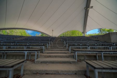 Empty seats at the stadium.Covered auditorium of a band shell in a park. Rows of audience benches in a bandshell (or stadium) under a protective filigree roof.  