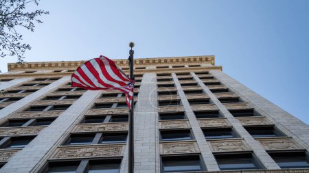merican flag fluttering in front of a classic high-rise building with intricate facade details.