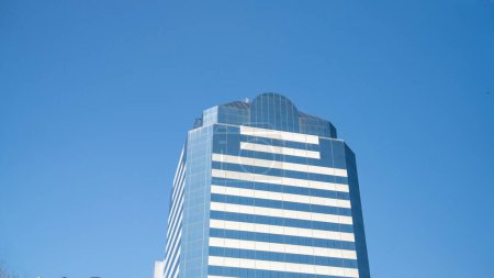 Moderner Wolkenkratzer mit reflektierender Glasfassade vor blauem Himmel.