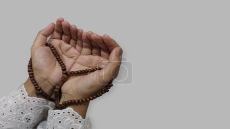 Muslim praying hands holding prayer beads in Ramadan, isolated gray background