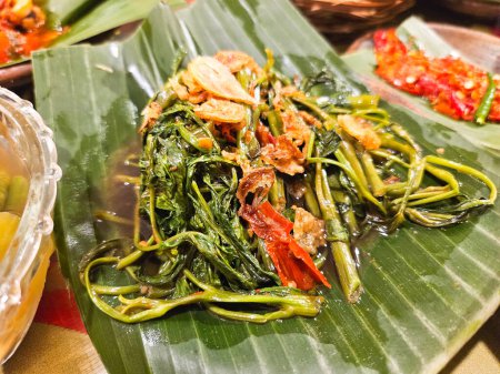 cah kangkung or Stir-fried Kale on an earthen plate with banana leaves, a traditional Indonesian food concept