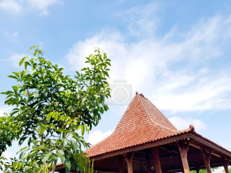 Banyumas, Indonesia - April 11, 2024 : A saung joglo roof with clouds and leaves in the background, at Mas kemambang, Banyumas, Indonesia