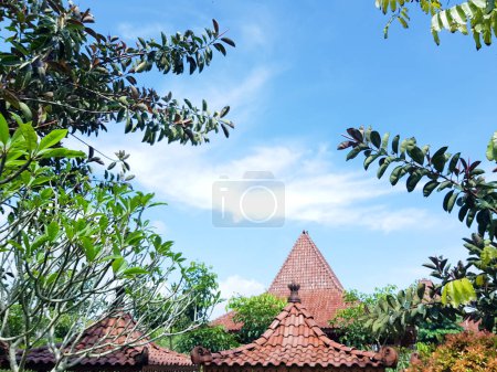 Photo for Banyumas, Indonesia - April 11, 2024 : A saung joglo roof with clouds and leaves in the background, at Mas kemambang, Banyumas, Indonesia - Royalty Free Image