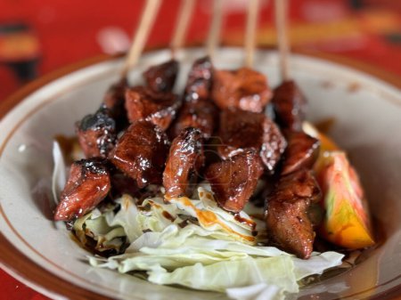 Sate kambing or lamb satay or goat meat satay served with sliced cabbage, tomatoes, sweet soy sauce and chilli, Indonesian street food