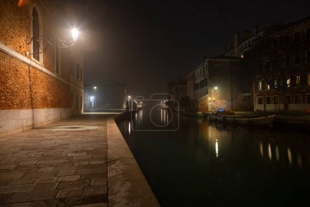 Esta es una imagen del canal que conduce al Arsenale, Venecia, Italia. La imagen fue tomada por la noche cuando la estructura y el área circundante fueron iluminados. El alumbrado público está silenciado debido al clima brumoso.