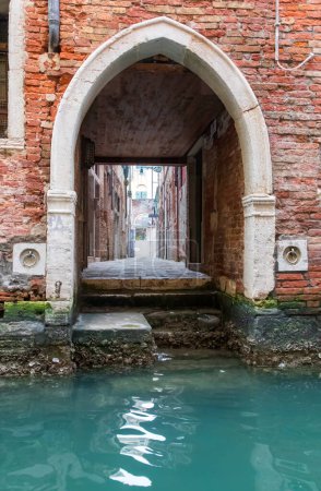 Image of an arched accessway from the canal straight onto a street in Venice . There a several steps and a standing area plus two mooring hooks.