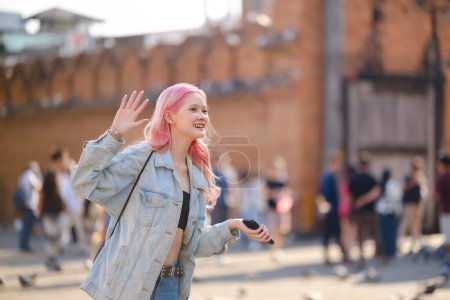 Women in pink hair style walking in the city waving hand say hi to other people. High quality.