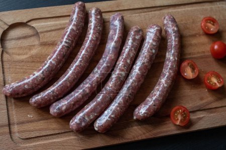 Raw sausages prepared for grilling, displayed on a wooden cutting board.