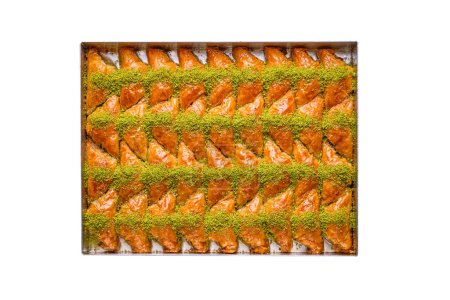 Téléchargez les photos : Un plateau de bonbons de baklava turcs, de forme triangulaire, farcis à la crème et décorés de pistaches, isolés sur un fond blanc - en image libre de droit
