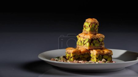 Foto de Un plato de dulces árabes con pistachos representados sobre fondo blanco y fondo gris y negro - Imagen libre de derechos