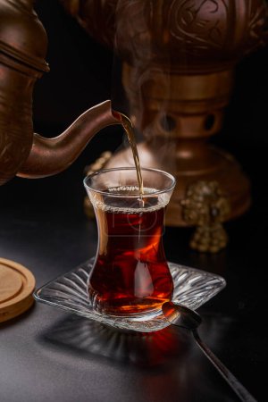 Close-up of a Turkish tea cup on a black background with copper utensils