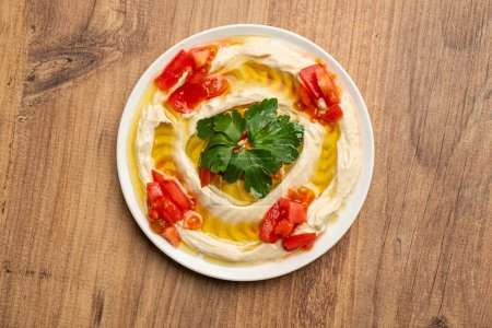 Top view photo of a plate of hummus with tahini and oil on a wooden floor