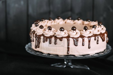 Foto de Primer plano de un delicioso pastel de chocolate con ganache de chocolate en un soporte de pastel de vidrio. El pastel se coloca en una mesa de madera oscura - Imagen libre de derechos