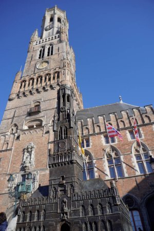 Ein kleines Modell des Glockenturms in Brügge, in einem Stadtzentrum mit einem echten Gebäude im Hintergrund an einem sonnigen Tag