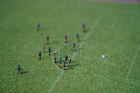 a group of people playing football on the ground on a minuature model railway diorama