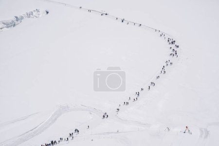 Foto de Vista lejana de muchas personas caminando en un sendero de nieve por un glaciar en los Alpes suizos. - Imagen libre de derechos