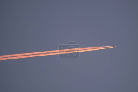 Téléchargez les photos : Avion dans le ciel avec une piste orange. Coucher de soleil - en image libre de droit