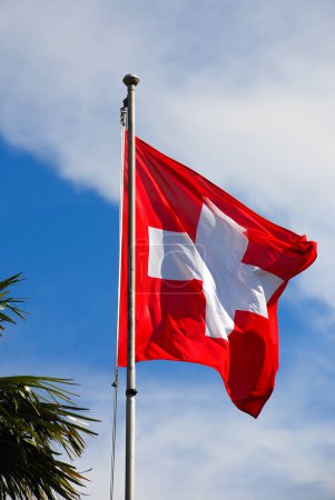 Téléchargez les photos : Le drapeau de la Suisse agite dans le vent contre le ciel bleu clair dans les nuages. - en image libre de droit