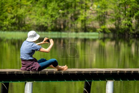 Téléchargez les photos : Une femme prend une photo sur une jetée au bord du lac. - en image libre de droit