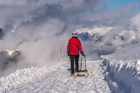 eine Person mit einem Schlitten macht sich bereit, den Berg in den Alpen hinunter zu fahren