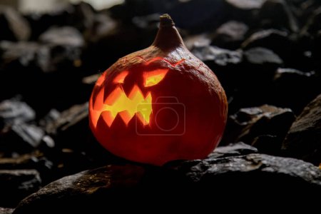 Téléchargez les photos : Une citrouille d'Halloween allumée avec une bougie et placée sur les pierres - en image libre de droit