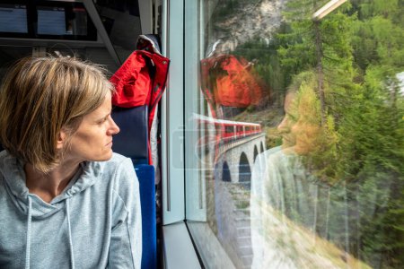 Frau blickt in Schweizer Alpen aus dem Fenster eines Zuges