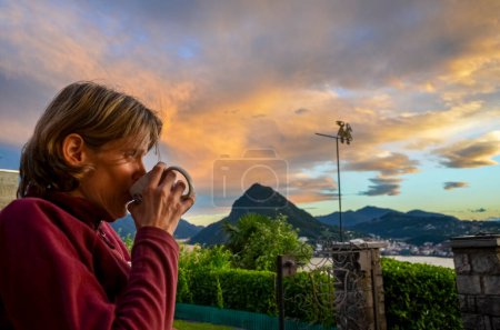 a woman drinks coffee on the top of a mountain at sunset.