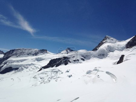 L'image montre une montagne enneigée en Suisse, face à un ciel bleu clair