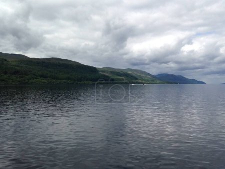 Das Bild zeigt ein Gewässer mit Hügeln im Hintergrund, das Loch Ness zeigt. Es zeigt eine ruhige Naturlandschaft mit bewölktem Himmel und einem friedlichen See.